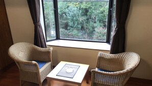 Een kamer met twee rieten stoelen, een klein tafeltje en een raam met uitzicht op groen.