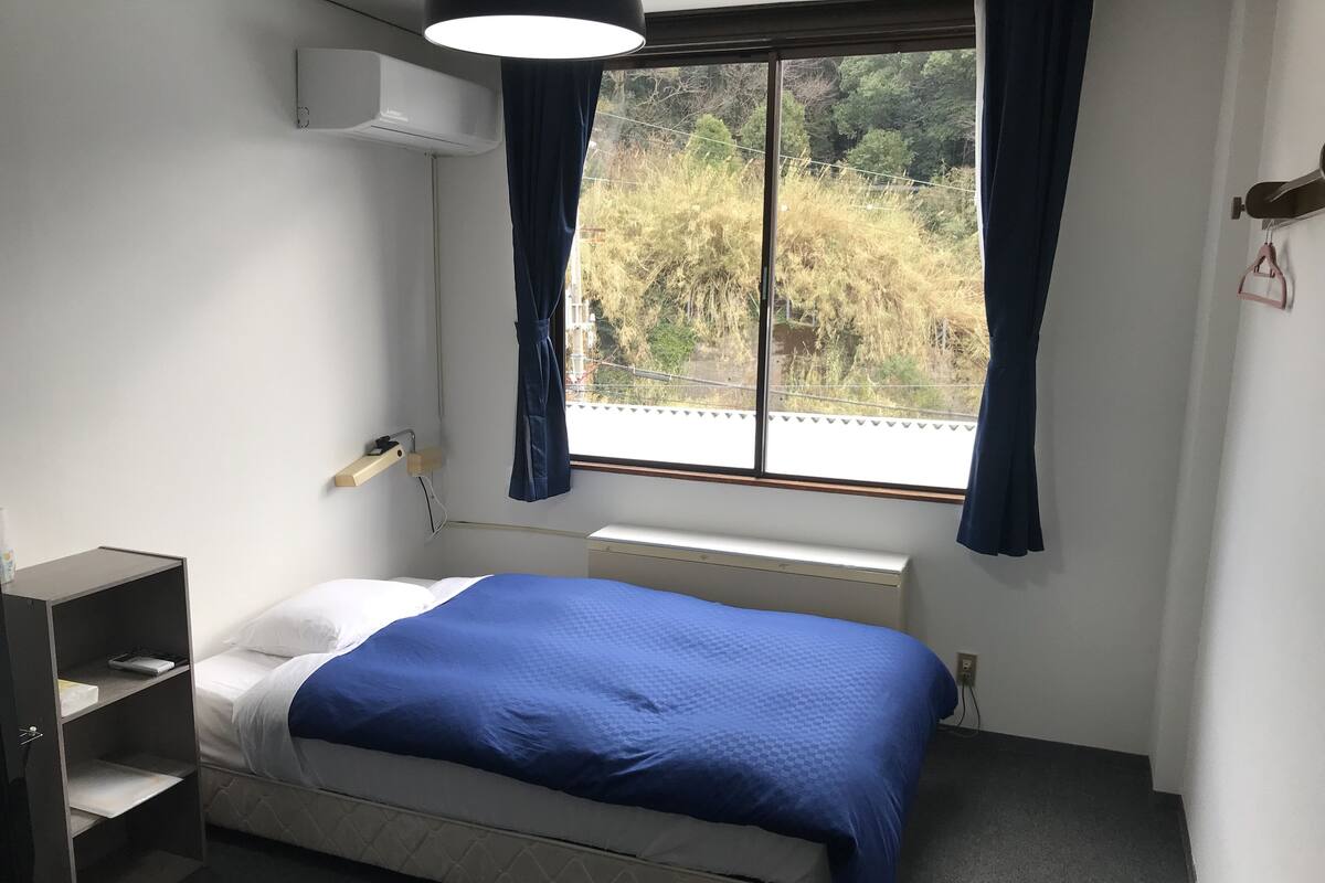 A bedroom with a bed, a desk, a window with curtains, and a radiator.