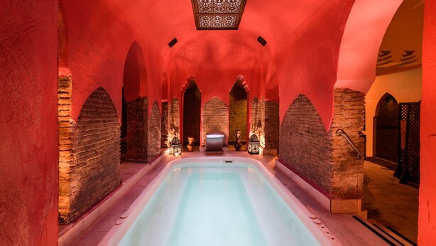 Uma área de spa com uma banheira de hidromassagem central, paredes de pedra e portas em arco.