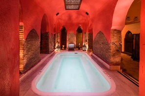 Un espace de bien-être doté d’un grand jacuzzi central, de murs en pierre et d’arcades.