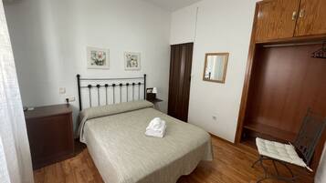 Un dormitorio con una cama, un armario de madera, una silla, una mesita de noche, un espejo y dos cuadros florales.