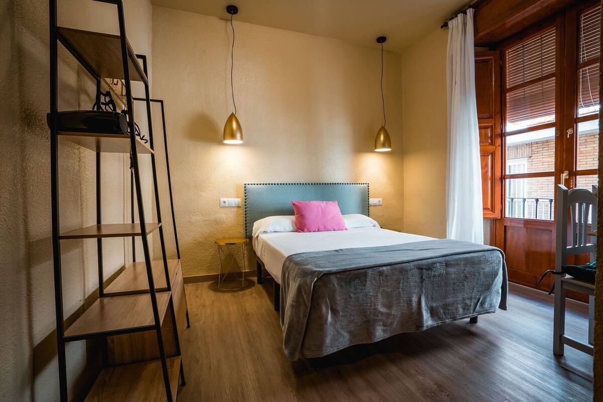 Ein Schlafzimmer mit einem Bett, einem Nachttisch, einer Holzleiter und zwei Pendelleuchten.