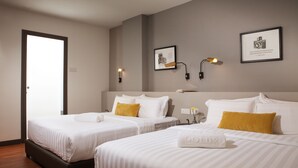 Una camera d'albergo con due letti, ognuno con biancheria da letto bianca e un cuscino giallo. Sono presenti luci a parete e quadri appesi.
