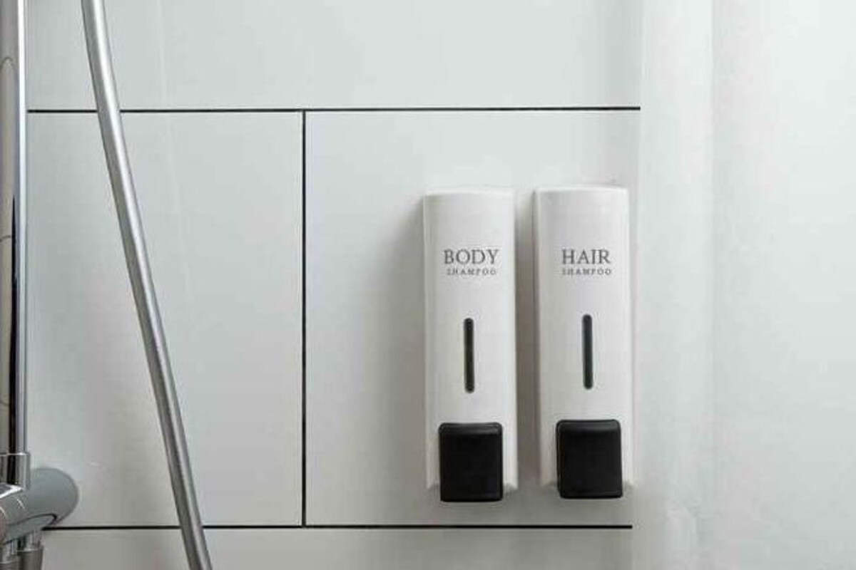A bathroom with two dispensers labeled 'BODY SHAMPOO' and 'HAIR SHAMPOO' mounted on the wall.