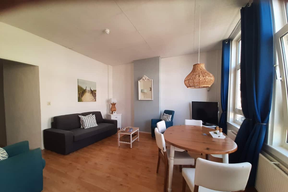 Een woonkamer met een bank, een eettafel met stoelen, een televisie en een raam met gordijnen.