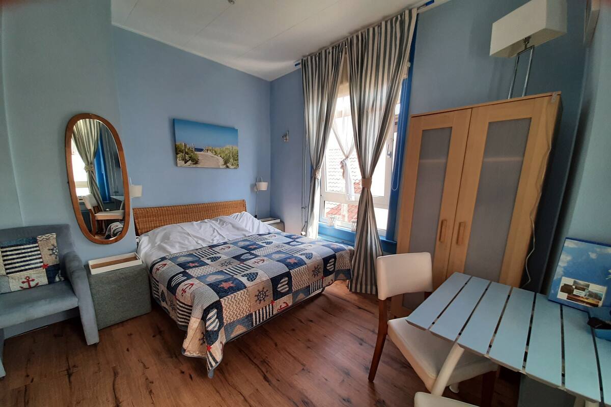 Een slaapkamer met een bed, een bureau, een stoel, een kledingkast en een raam met gordijnen.