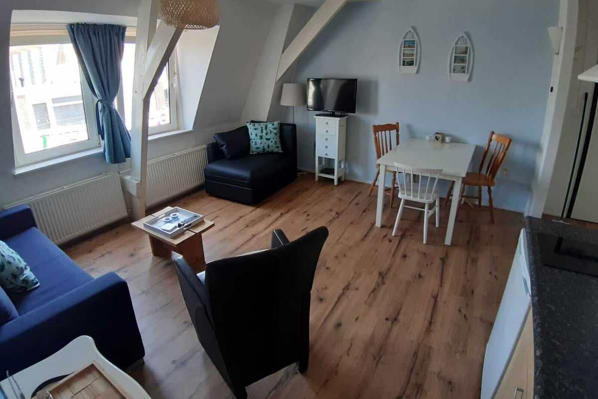 Een gezellige woonkamer met een bank, een eettafel met stoelen, een televisie en een lamp.