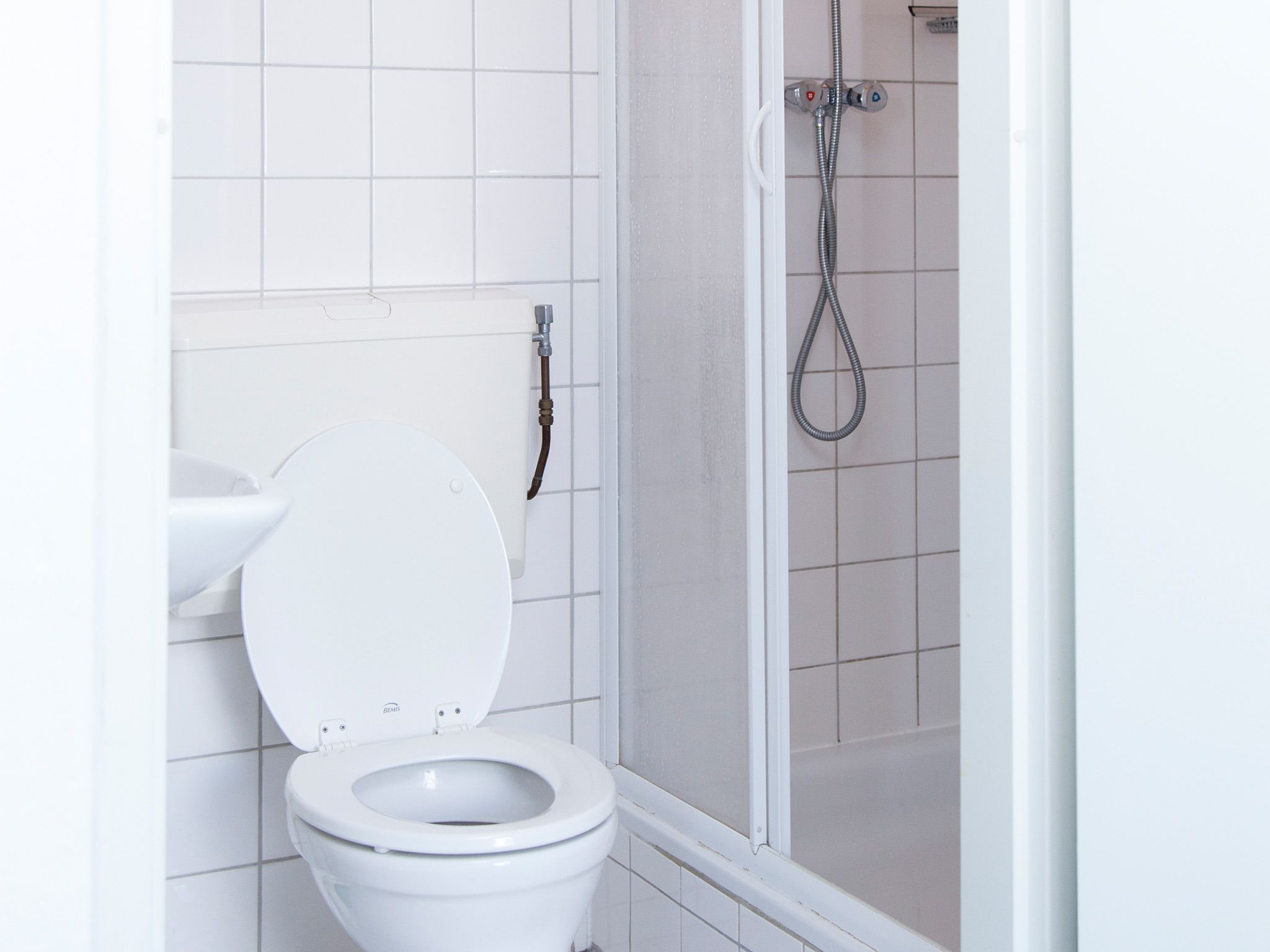 Kylpyhuone, jossa on valkoinen wc-istuin, lasiovilla varustettu suihku ja pesuallas.