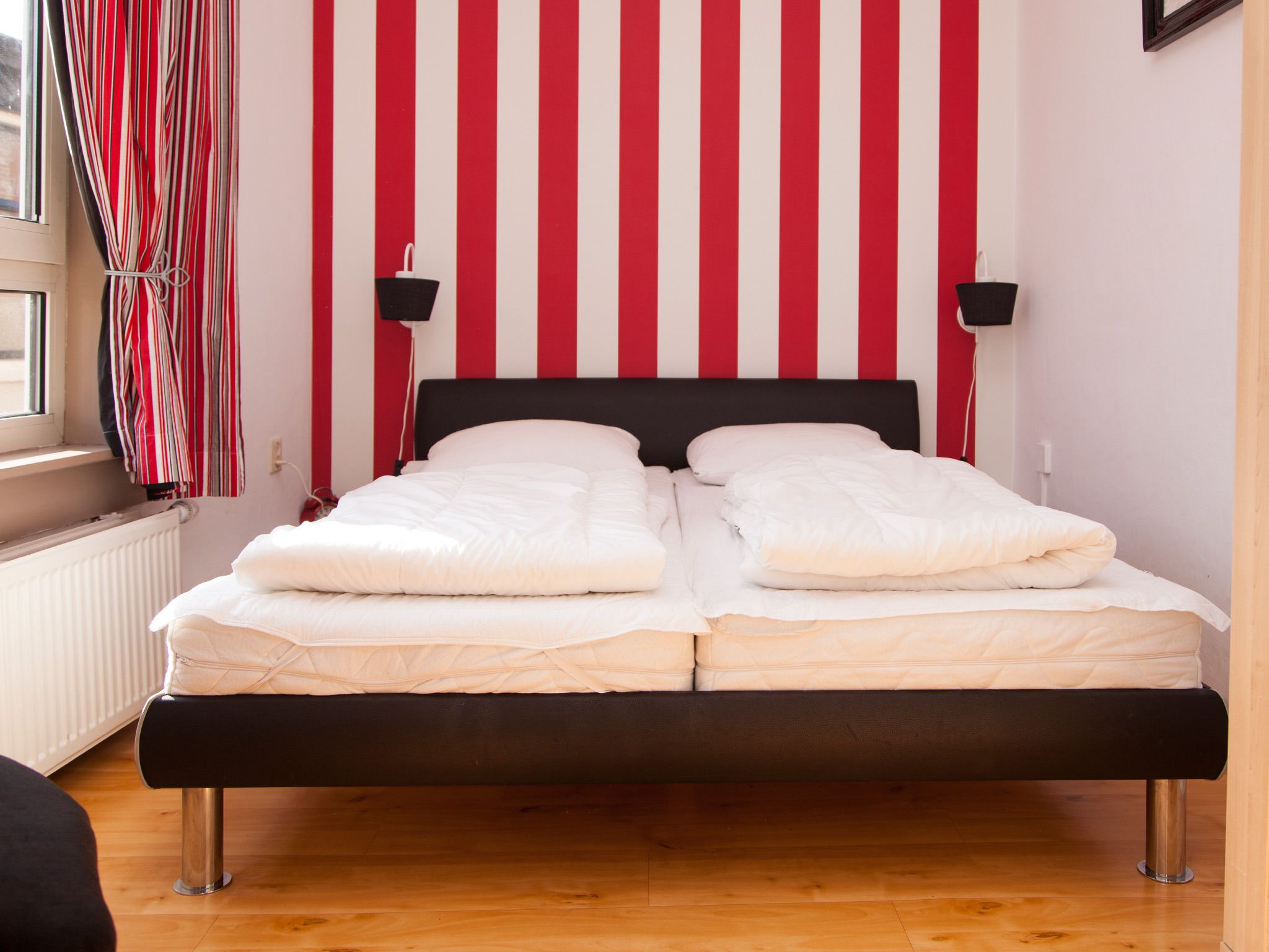 A bed with a black frame and white bedding, a red and white striped wall, and two bedside lamps.