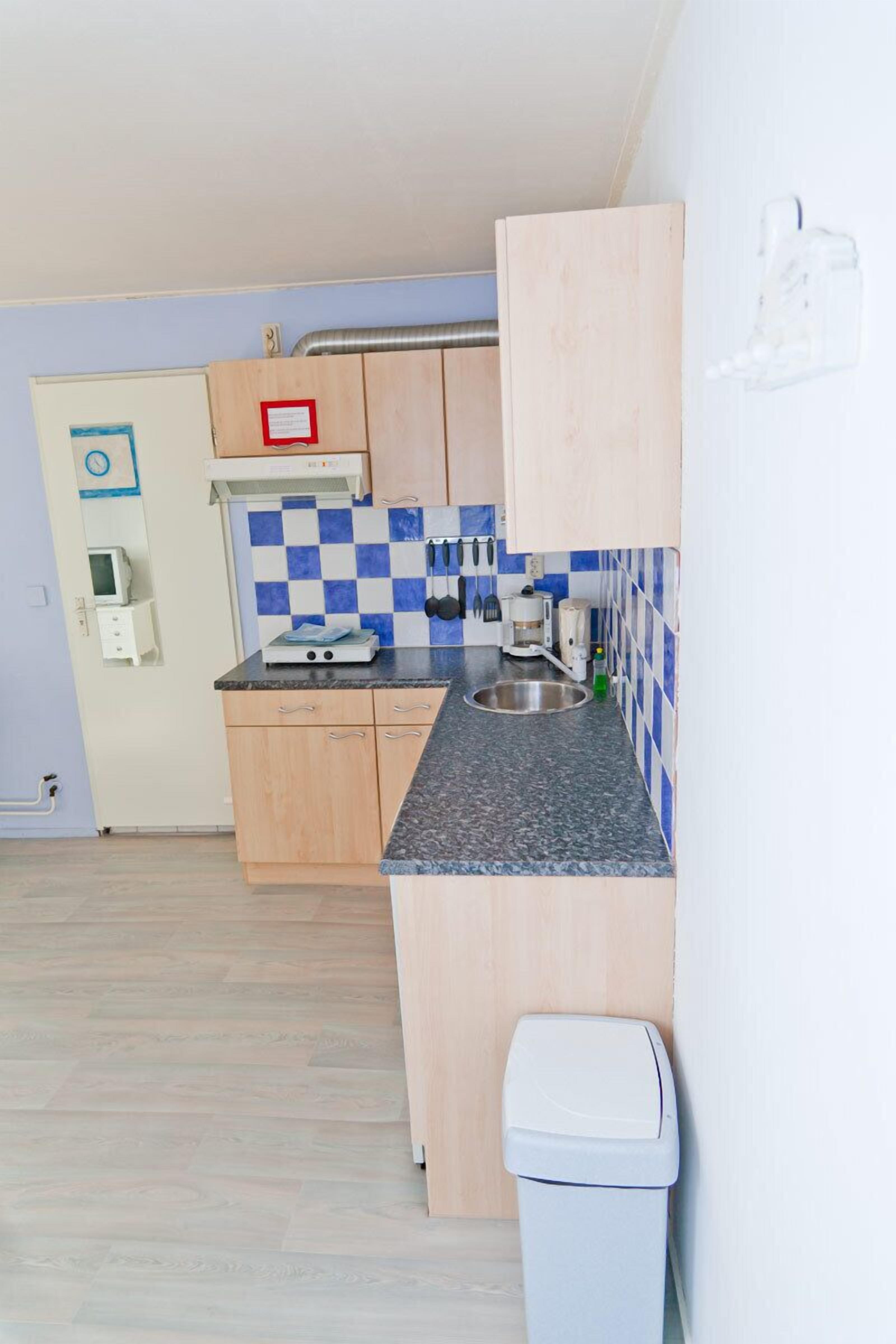 Een kleine keuken met een zwart-wit geruit spatwand, een magnetron, een koffiezetapparaat en een prullenbak.