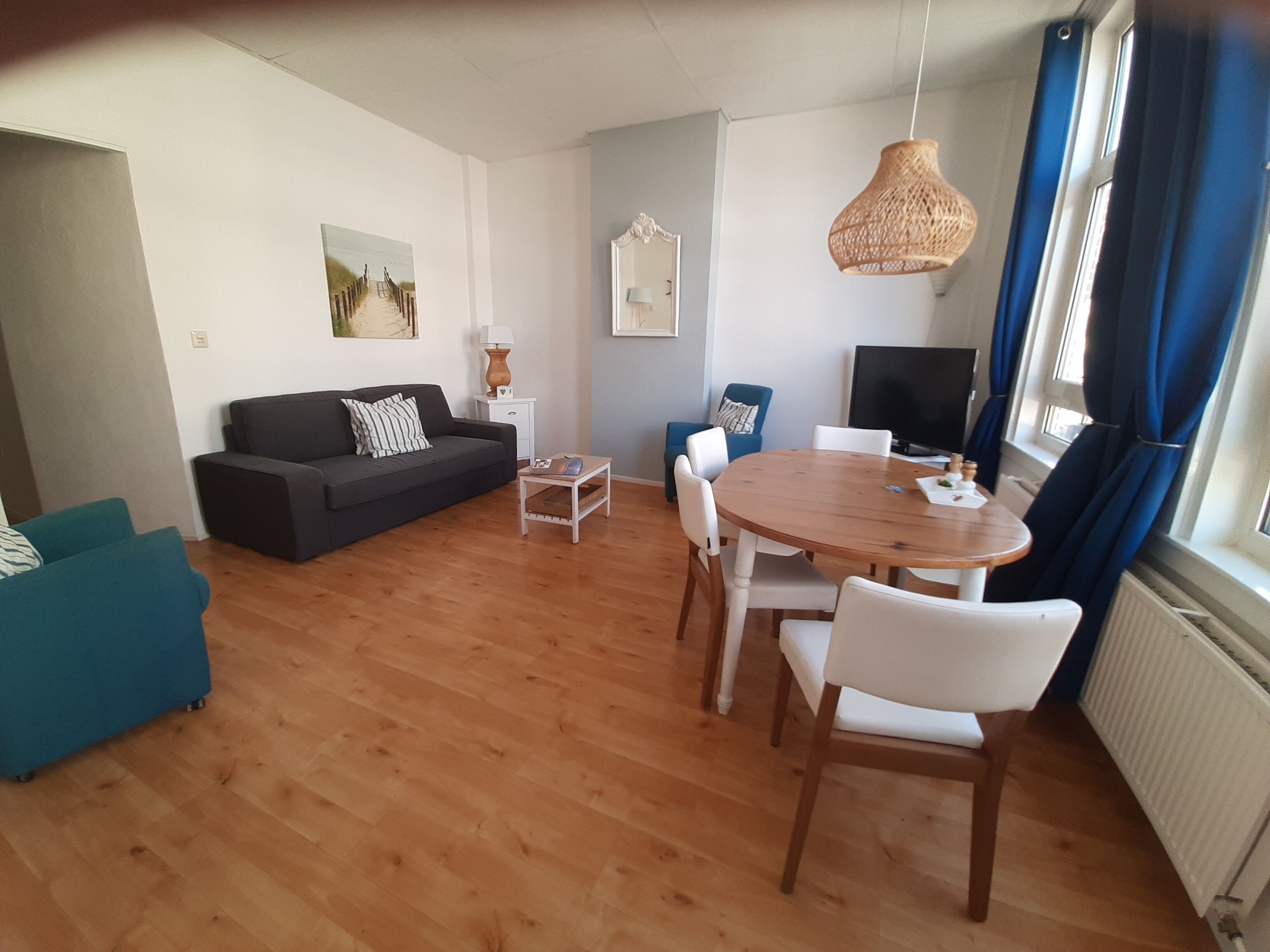 Un salon moderne avec une table à manger en bois, des chaises blanches, un canapé noir et un fauteuil bleu.