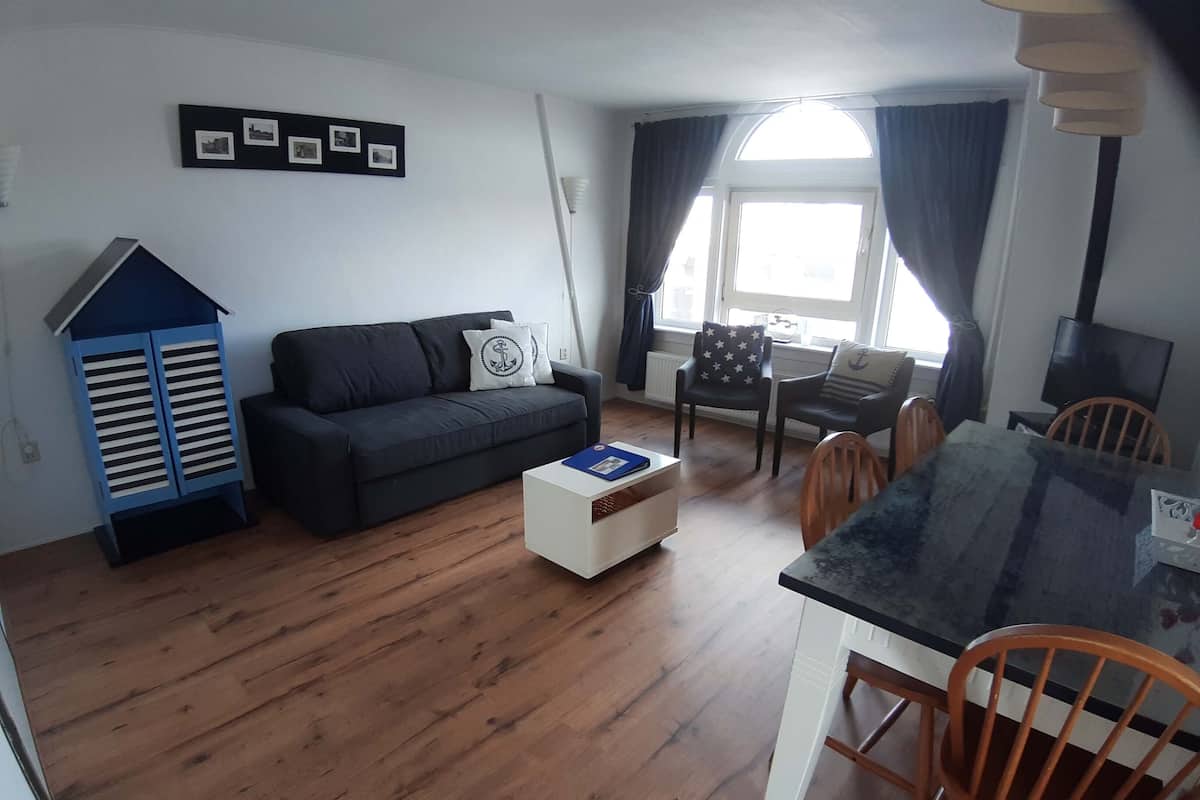 Een woonkamer met een bank, een salontafel, een eettafel met stoelen, een televisie en een raam met gordijnen.