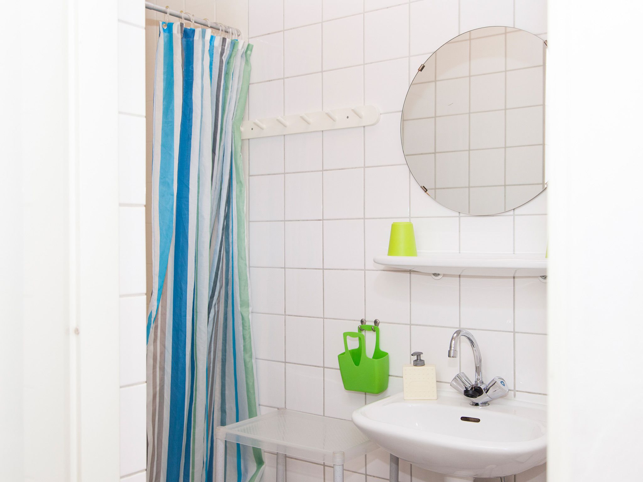 A bathroom with a shower curtain, a sink, a mirror, and a green bag on a shelf.
