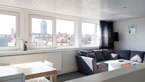 Un salon moderne avec un plafond blanc, de grandes fenêtres, un canapé gris, une table blanche et un radiateur.