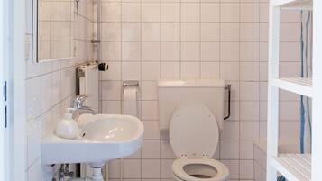 Une salle de bain avec un lavabo, des toilettes et une douche, le tout de couleur blanche.