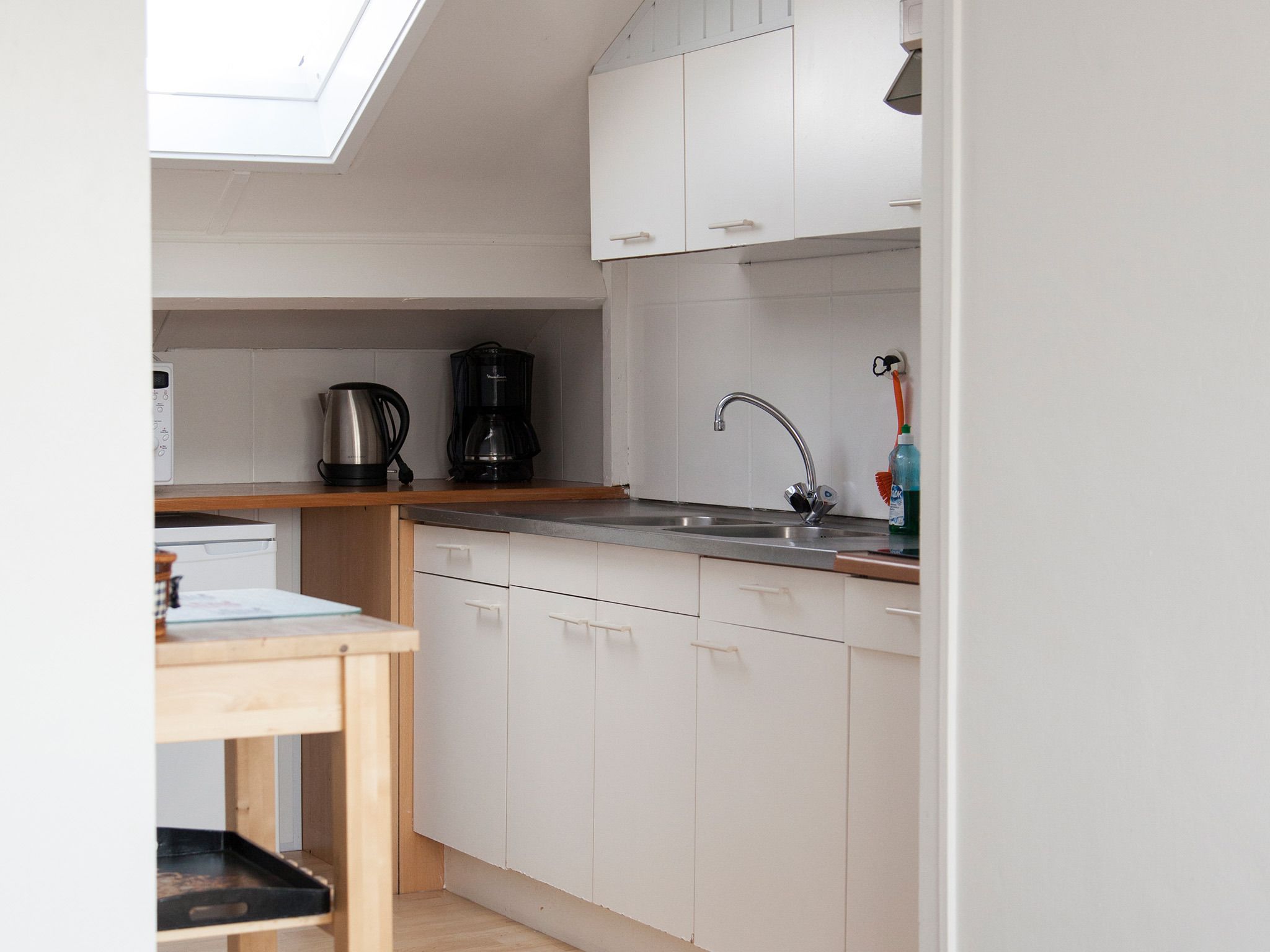 A compact kitchen with white cabinets, a stainless steel sink, and a coffee maker.