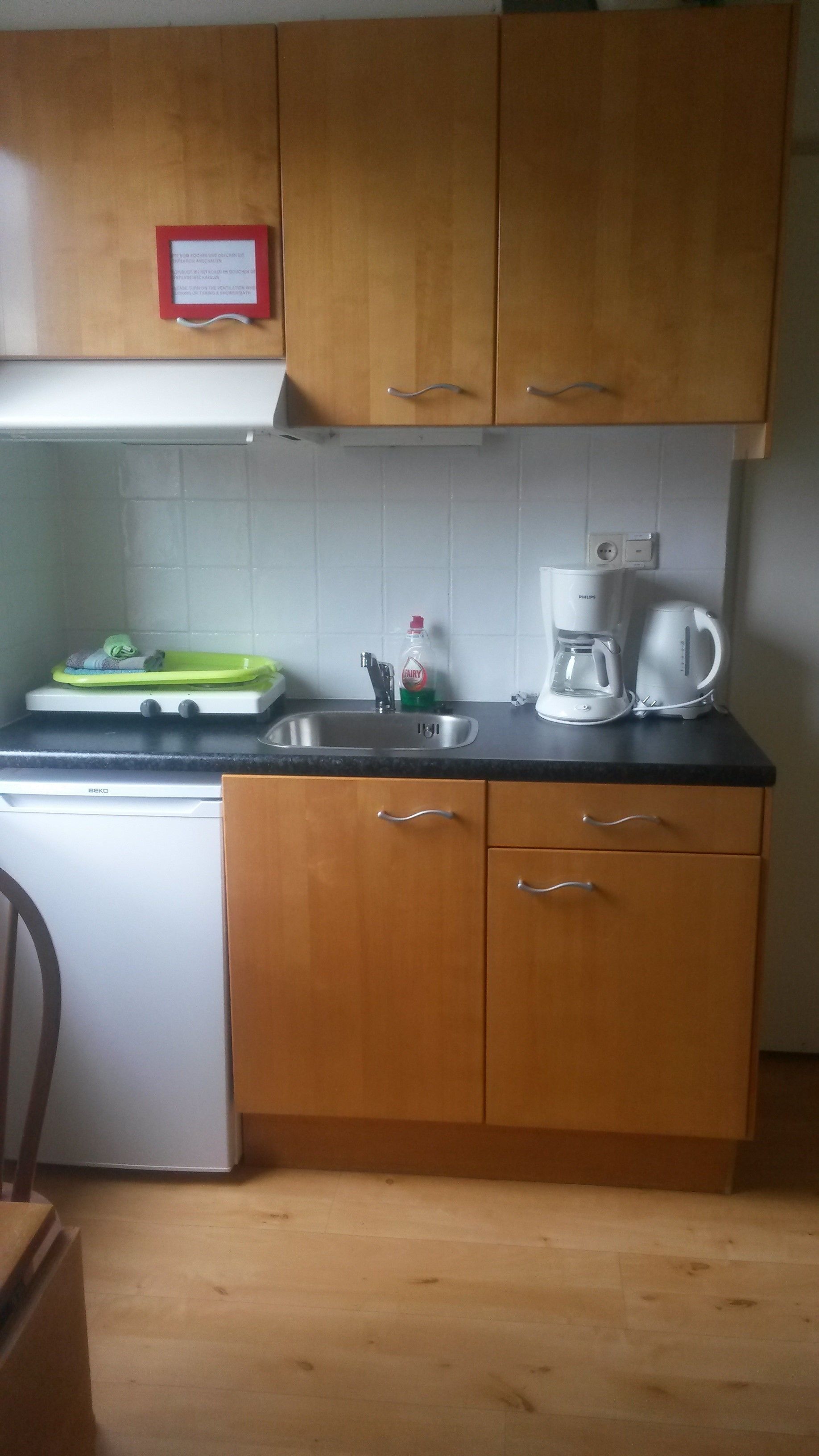 A kitchen with wooden cabinets, a sink, a kettle, and a dish rack.
