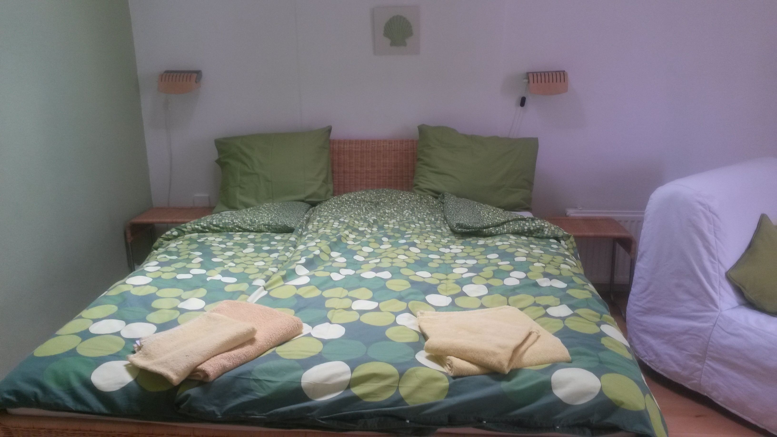 A bed with a green and white polka dot bedspread, two pillows, and two folded towels.
