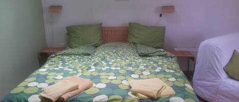 A bed with a green and white polka dot bedspread, two pillows, and two folded towels.