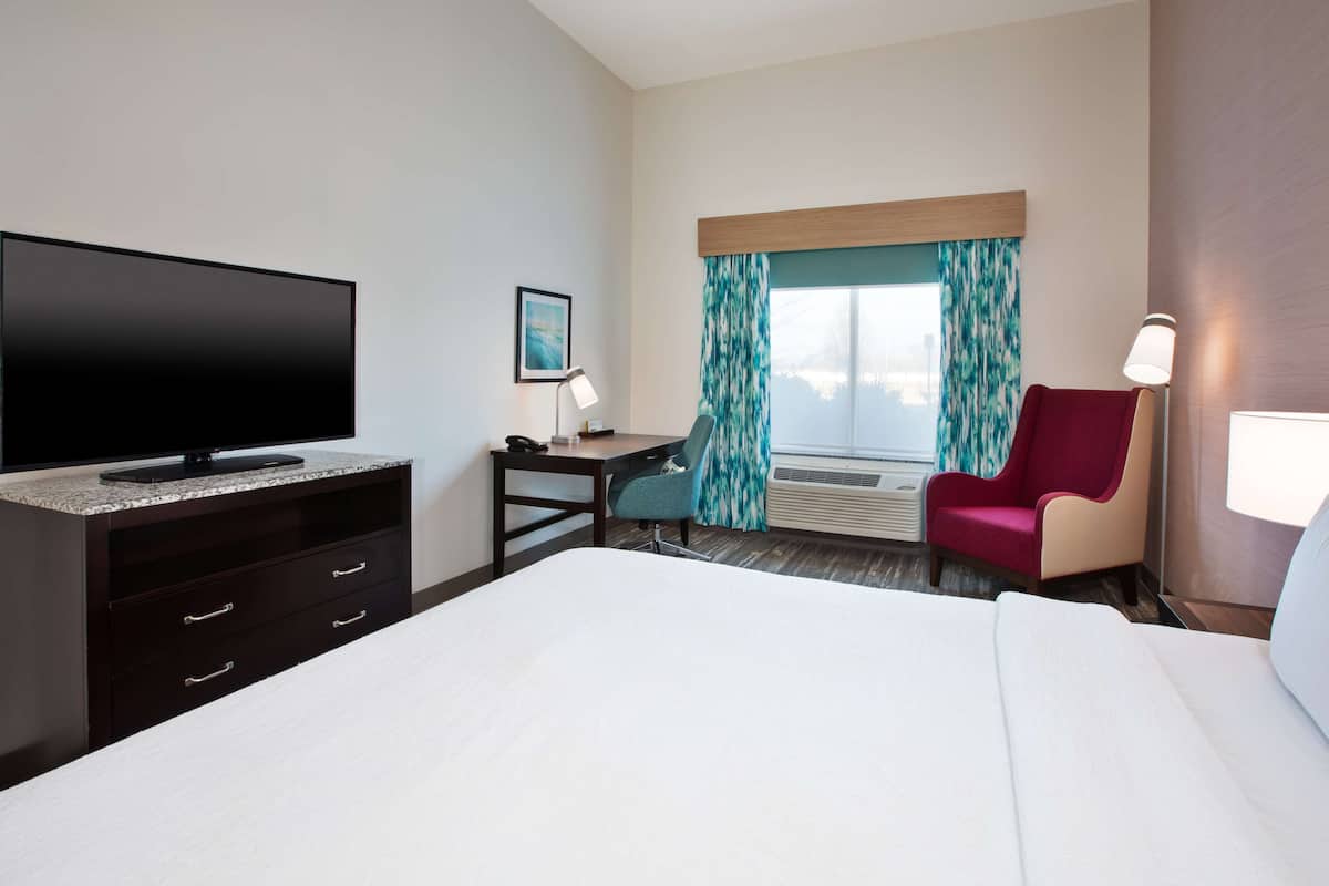 Una habitación de hotel con una cama grande, un escritorio con una computadora, un televisor y una silla.
