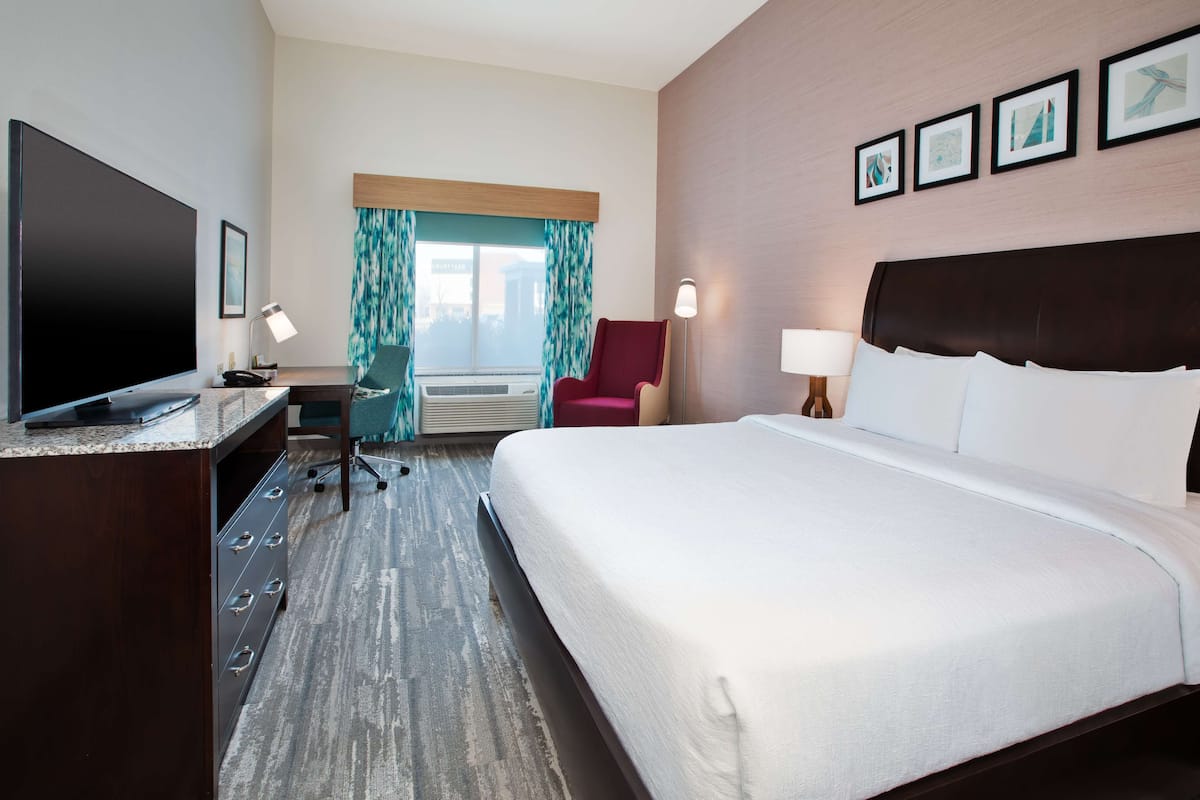 Habitación de hotel con una cama grande, un escritorio con televisor de pantalla plana, una silla y una ventana con cortinas.