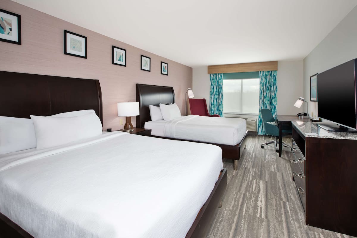Habitación de hotel con dos camas, un escritorio, un televisor y una ventana con cortinas.