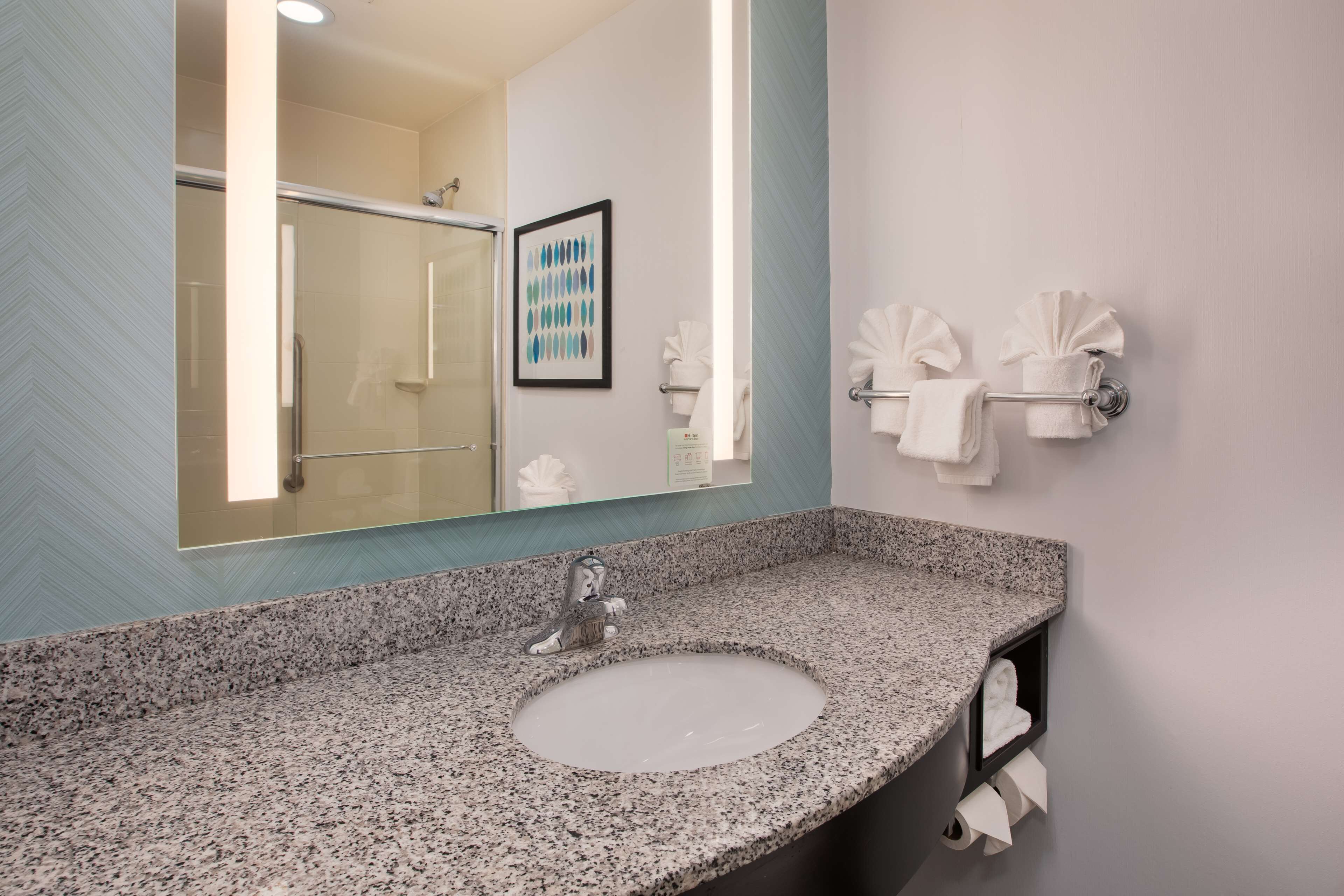 A bathroom with a granite countertop sink, a large mirror, and a towel rack with folded towels.