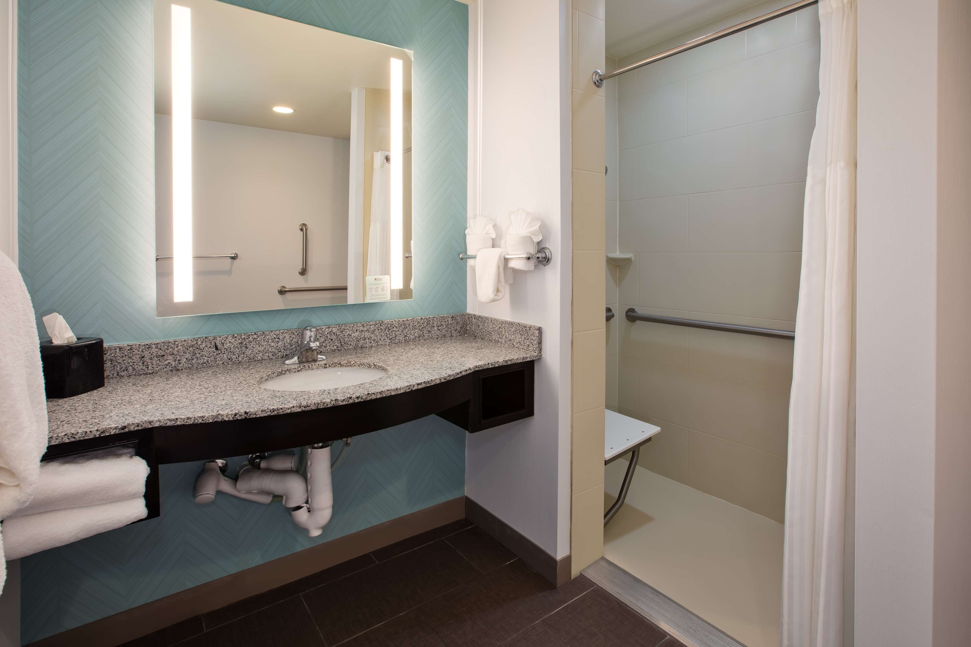 A modern bathroom with a granite countertop sink, a large mirror, and a walk-in shower.