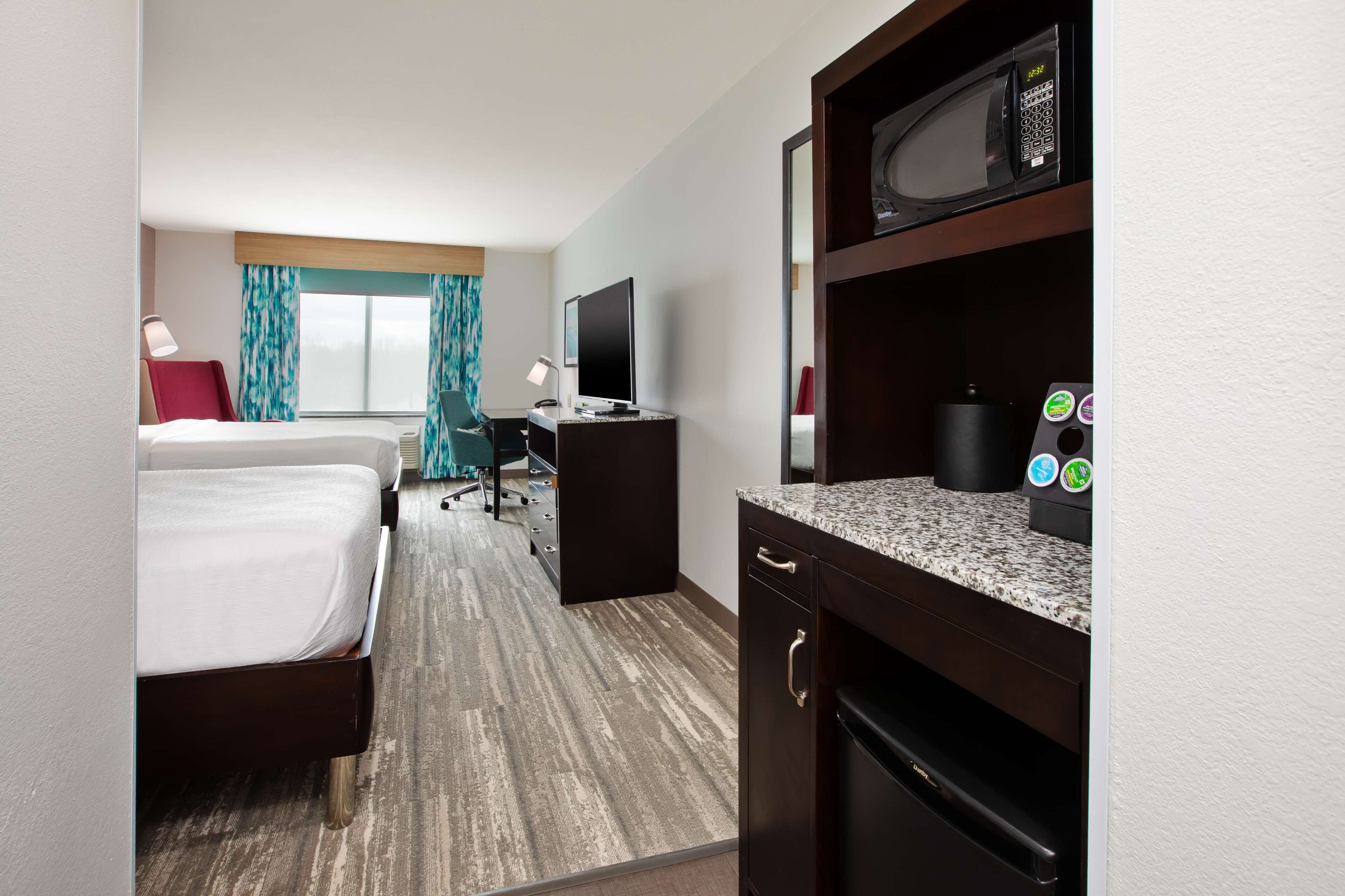 A hotel room with a bed, desk, television, microwave, and a coffee machine.