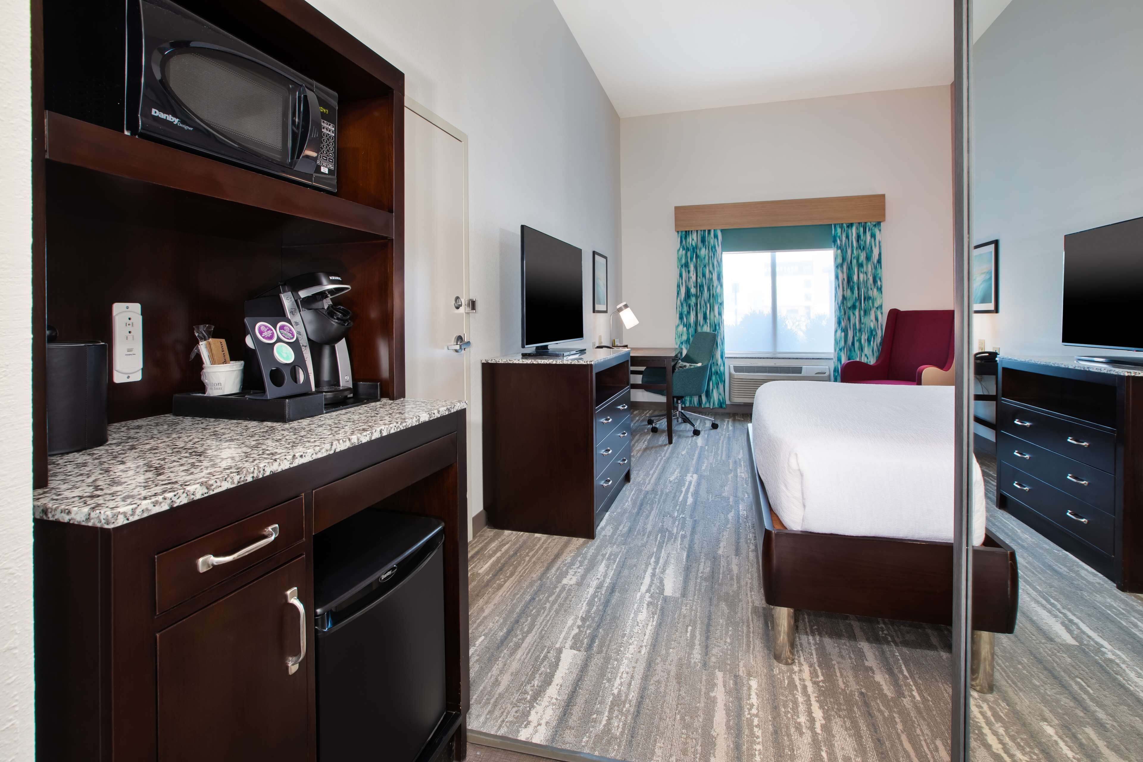 Habitación de hotel con una cama, un escritorio con computadora, un microondas y una cafetera.