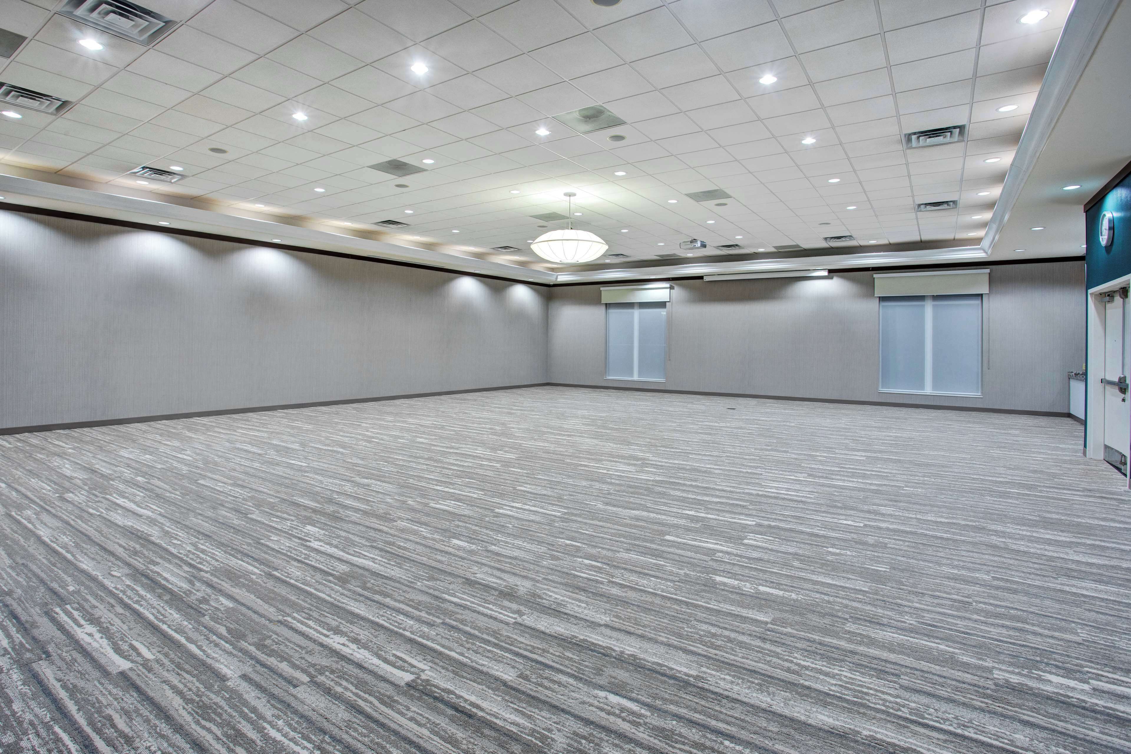 Un amplio salón de conferencias vacío con alfombra estampada, iluminación empotrada y un candelabro.
