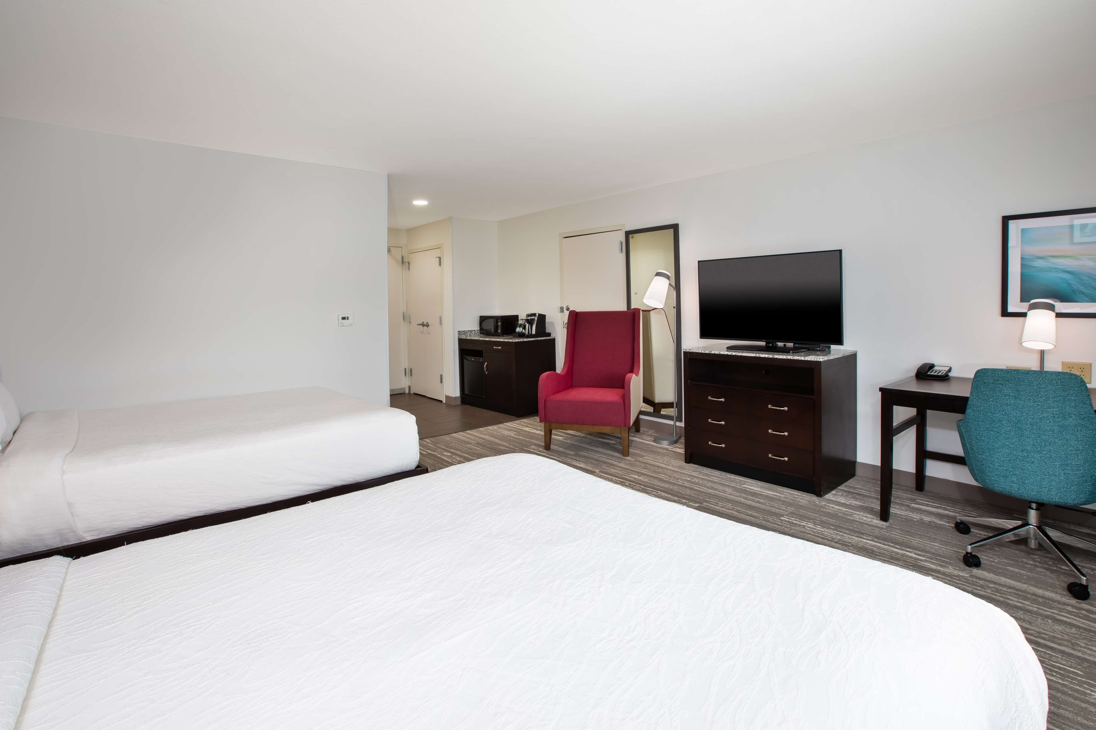Une chambre d’hôtel avec deux lits, une télévision, un bureau avec une chaise et un fauteuil rouge.