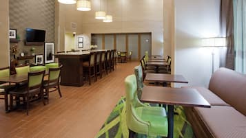 Un vestíbulo de hotel con una zona de bar, arreglos de asientos y un televisor montado en la pared.