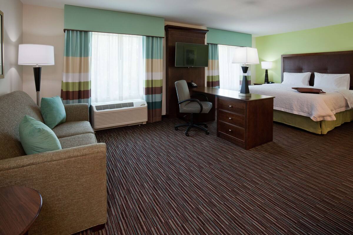 A hotel room with a sofa, a desk with a chair, a bed, and a television.