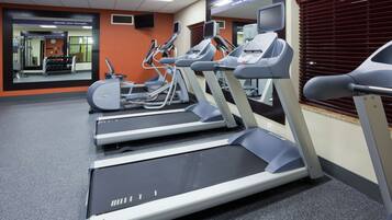 Une salle de sport équipée de tapis de course, de vélos elliptiques et d’un mur recouvert de miroirs.