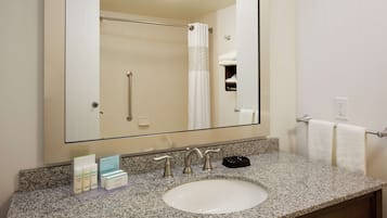 A bathroom with a large mirror, a granite countertop, a sink, and a towel rack.