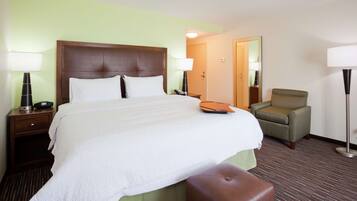 A hotel room with a large bed, a bedside table with a lamp, a chair, and a mirror.