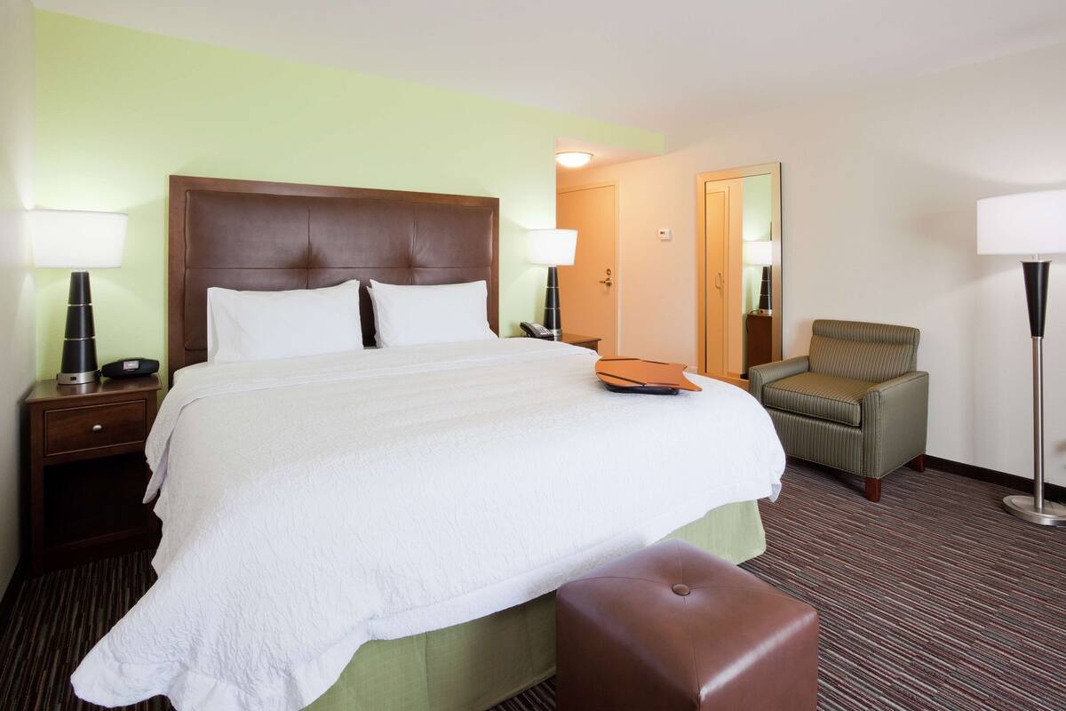 A hotel room with a large bed, a bedside table with a lamp, a chair, and a floor lamp.