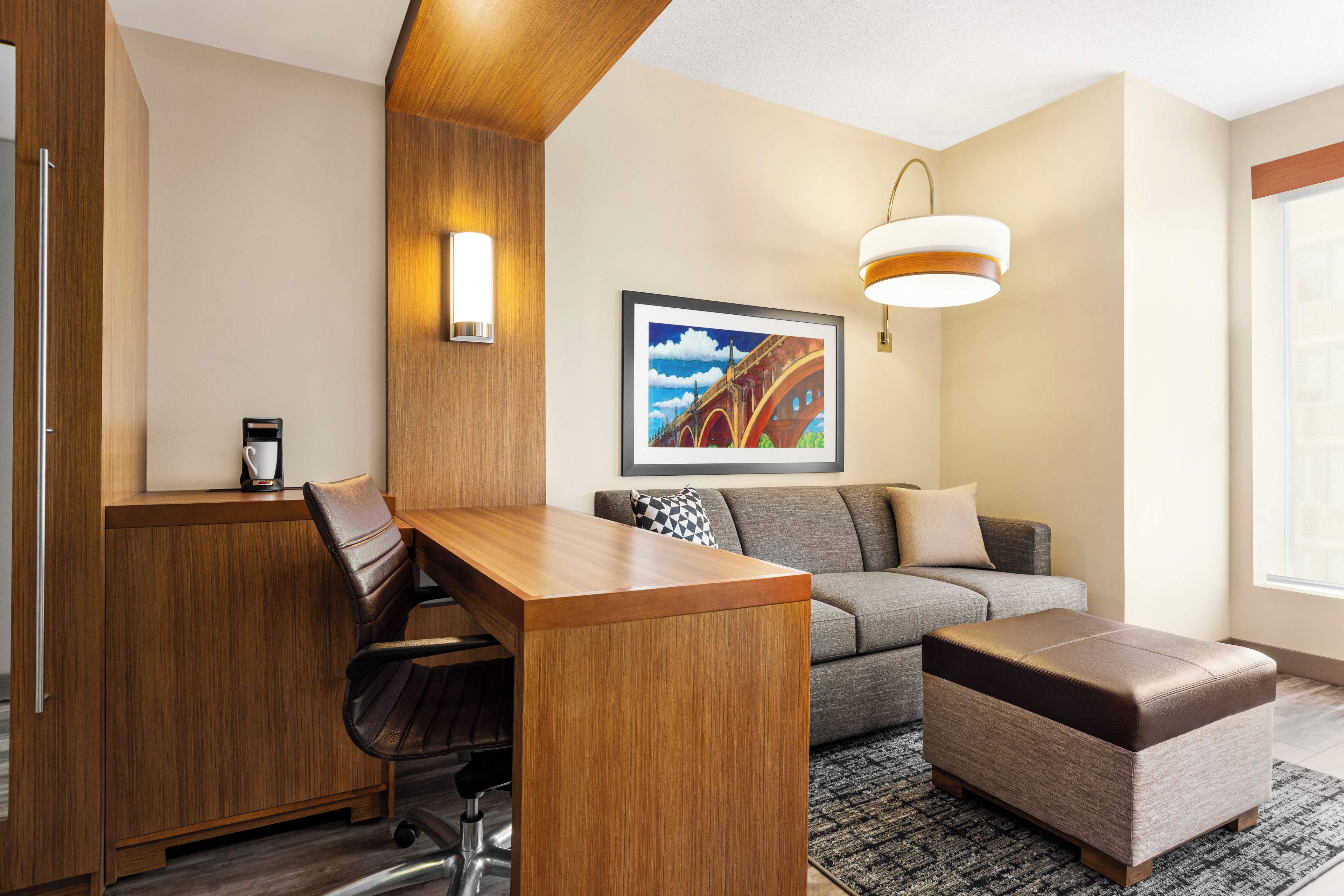 A modern room with a wooden desk, a sofa, a cushioned bench, and a framed painting on the wall.