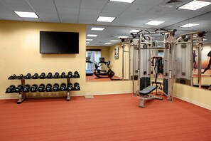 A gym with weightlifting equipment, a mirror, and a television on the wall.