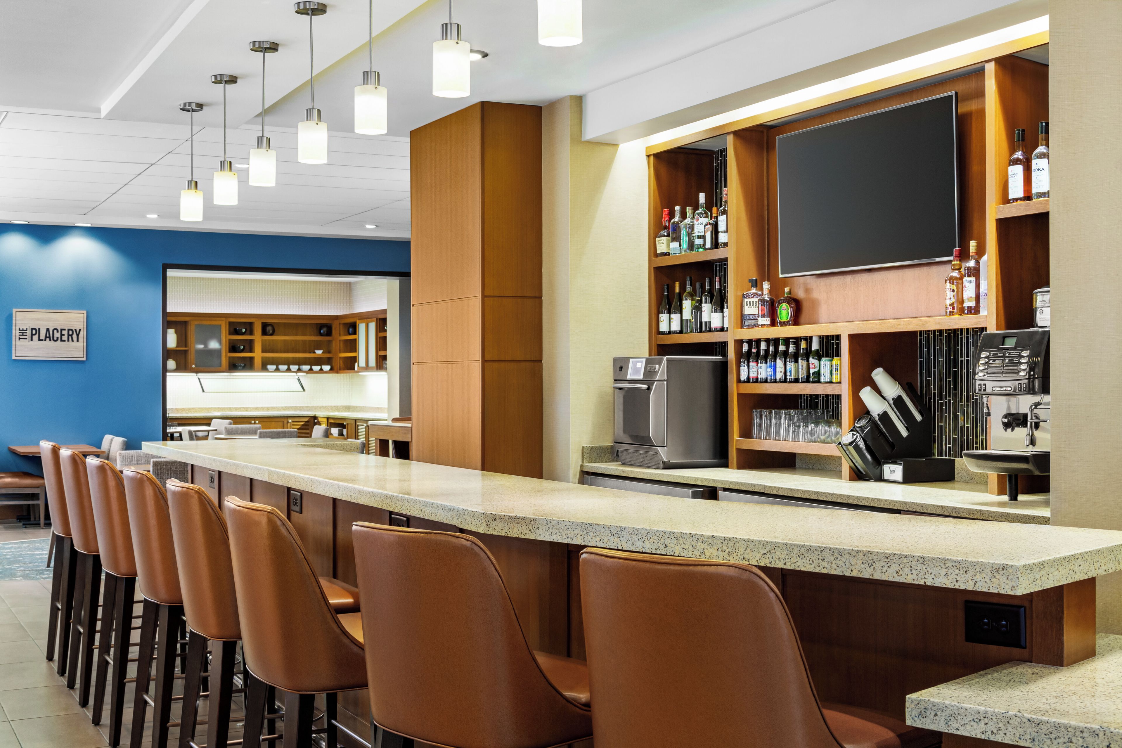 A bar area with a long counter, multiple bar stools, and a variety of liquor bottles.