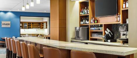 A bar area with a long counter, multiple bar stools, and a variety of liquor bottles.