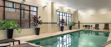 Una piscina interior con agua cristalina, rodeada de sillas de descanso y plantas en macetas.