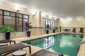 Una piscina interior con agua cristalina, rodeada de sillas de descanso y plantas en macetas.