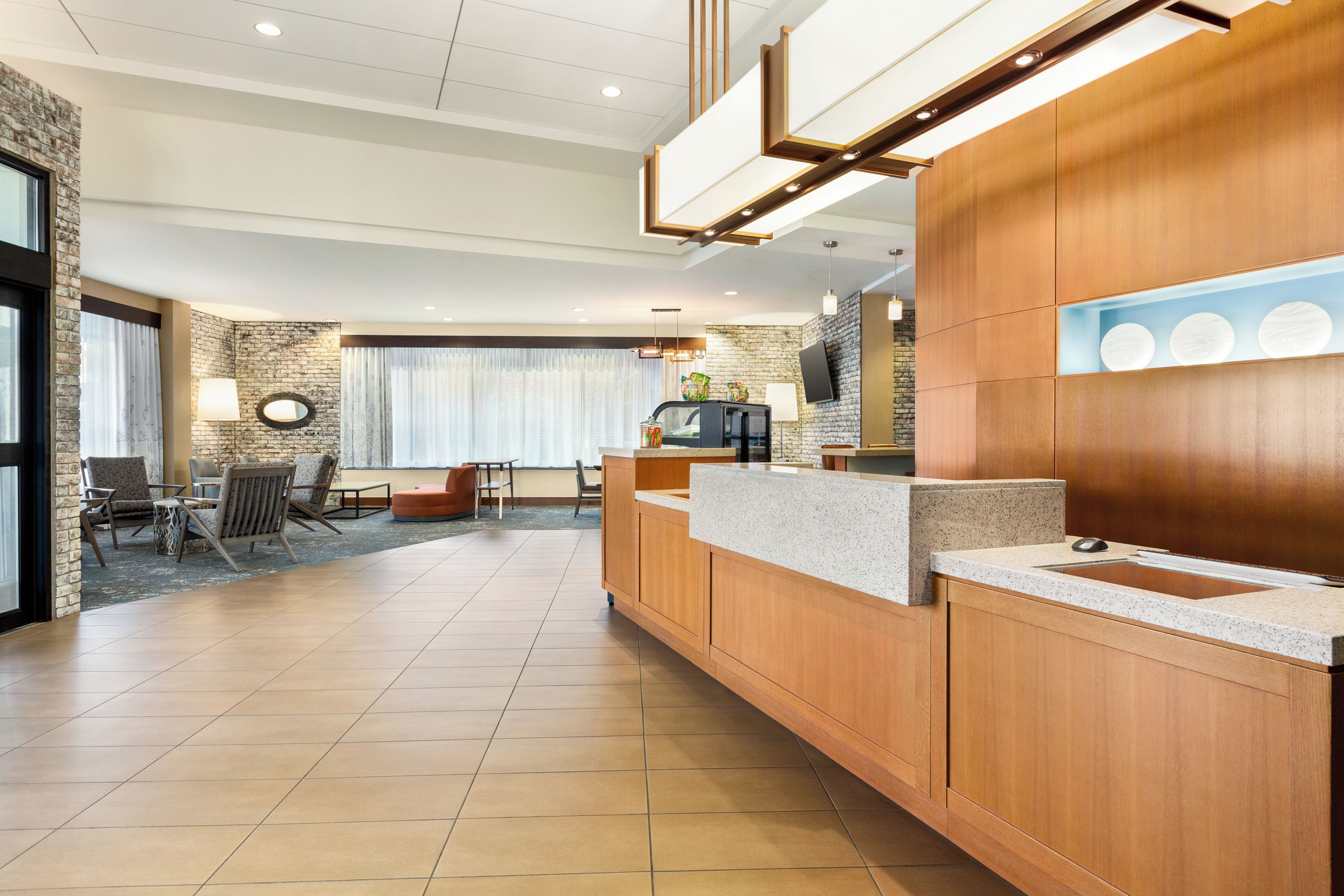 A modern hotel lobby with a reception desk, seating area, and a large window with curtains.