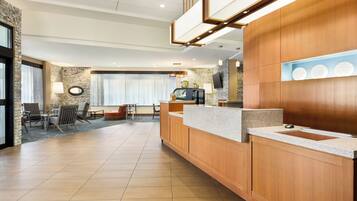 A modern hotel lobby with a reception desk, seating area, and a large window with curtains.