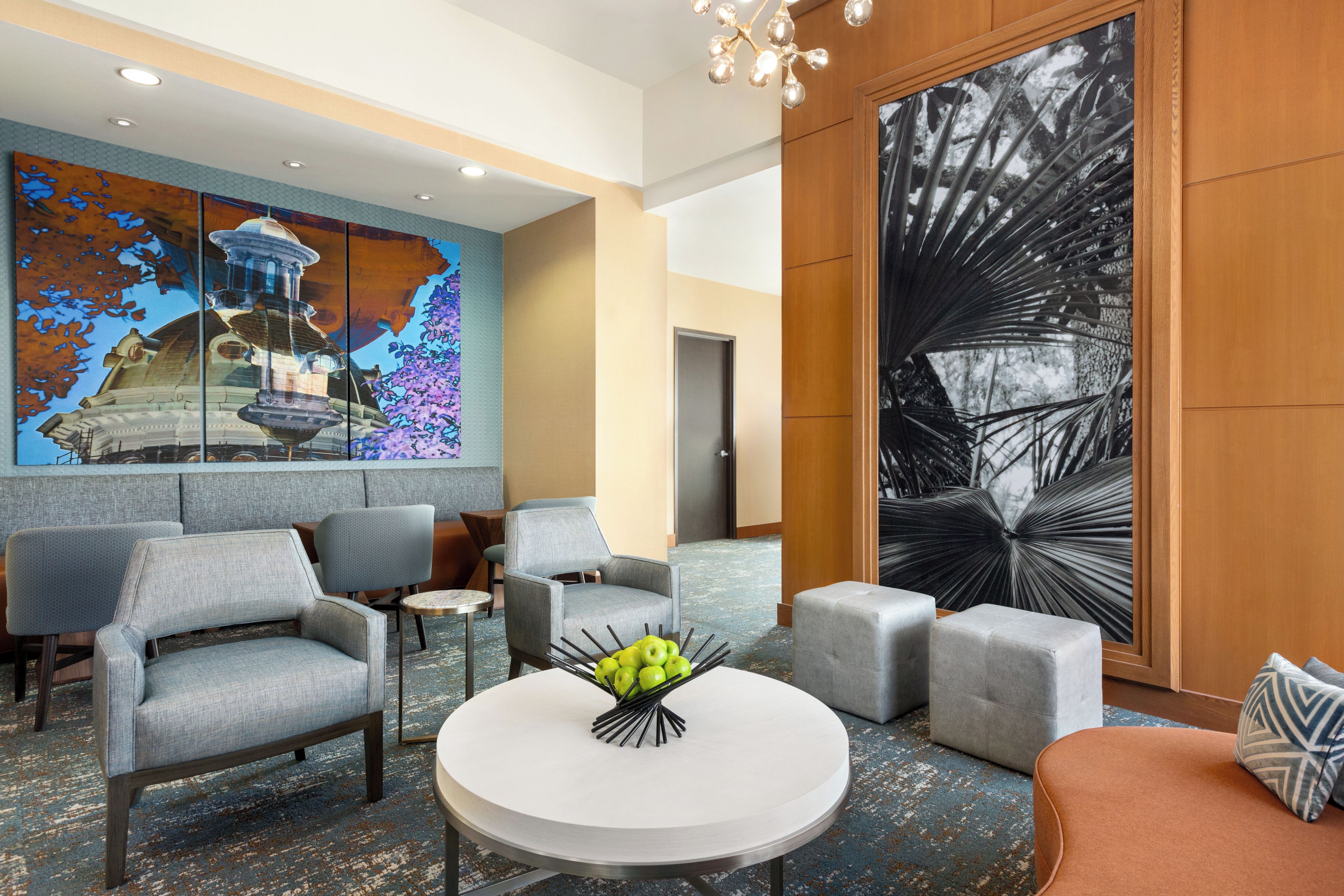 A lobby with modern furniture, a round table with a fruit centerpiece, and large abstract wall art.