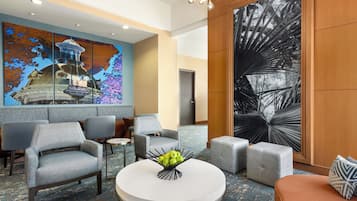 Um hall com móveis modernos, uma mesa redonda com arranjo de frutas e grandes obras de arte abstratas nas paredes.
