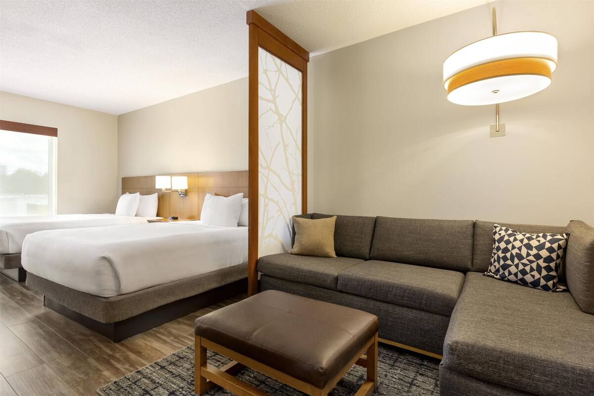 Een hotelkamer met twee bedden, een bank, een houten bankje en een moderne plafondlamp.