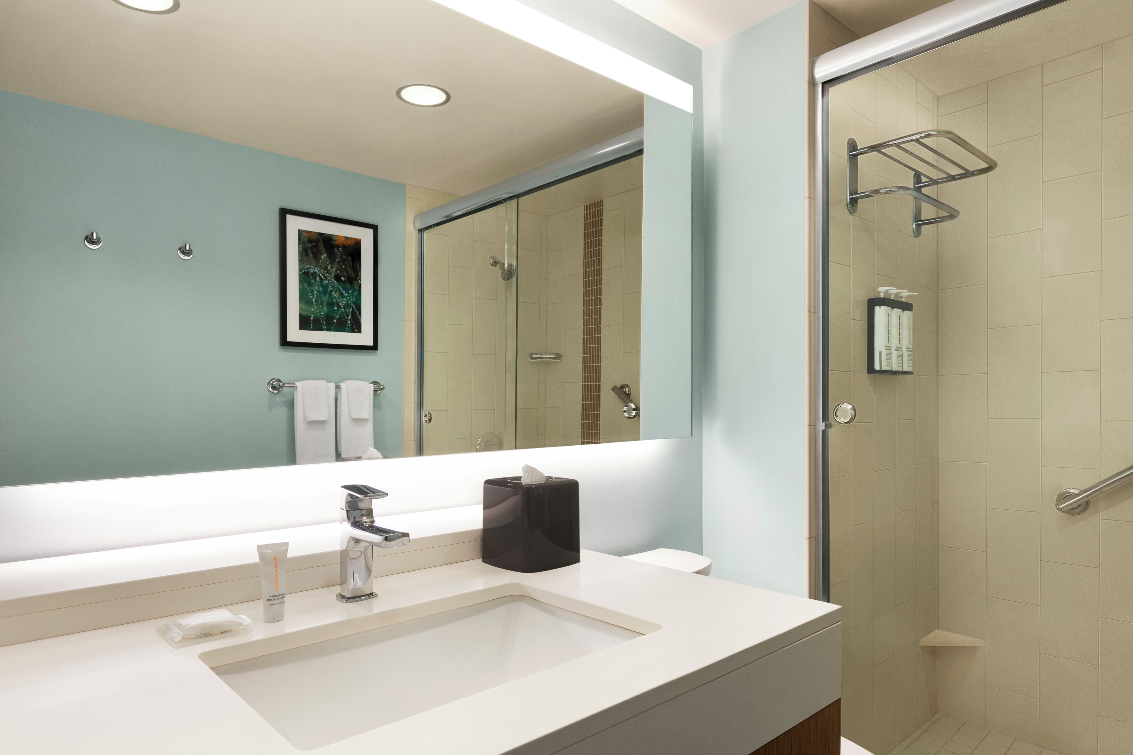 Un baño moderno con un espejo grande, un lavabo y una ducha con cerramiento de vidrio.